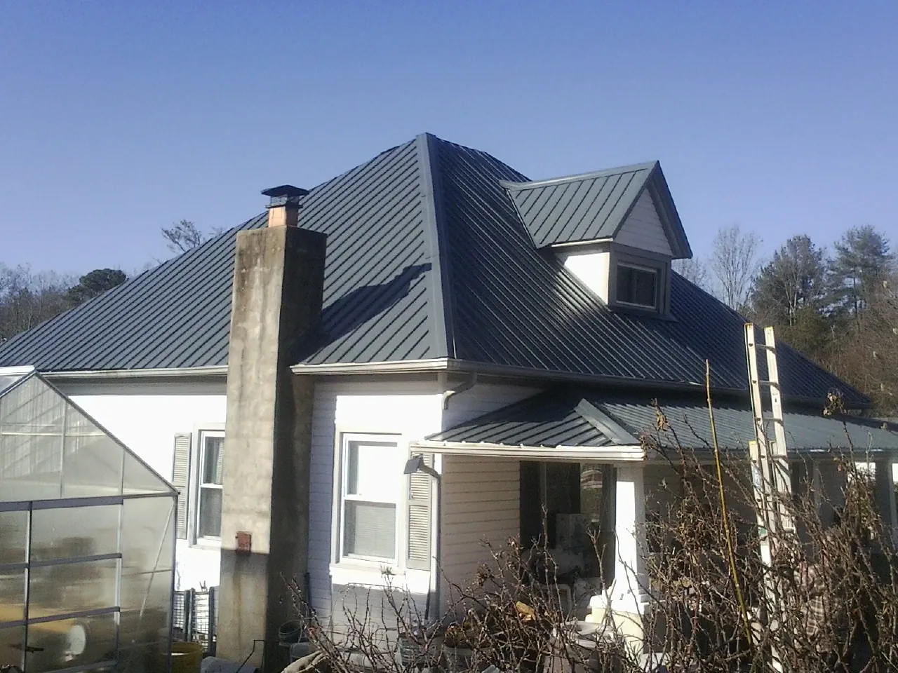 Dark blue standing seam metal roof on a white farmhouse with dormer — Slate & Tile Roof Repair by Roofing Brothers in Scottsville