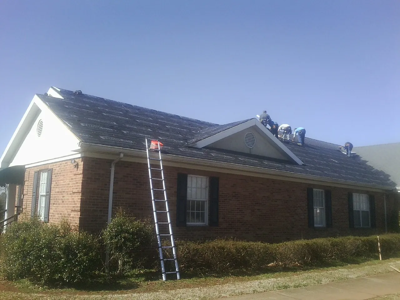 Crew tearing shingles off a brick ranch roof with a ladder set — Metal Roof Repair work by our crew in Scottsville