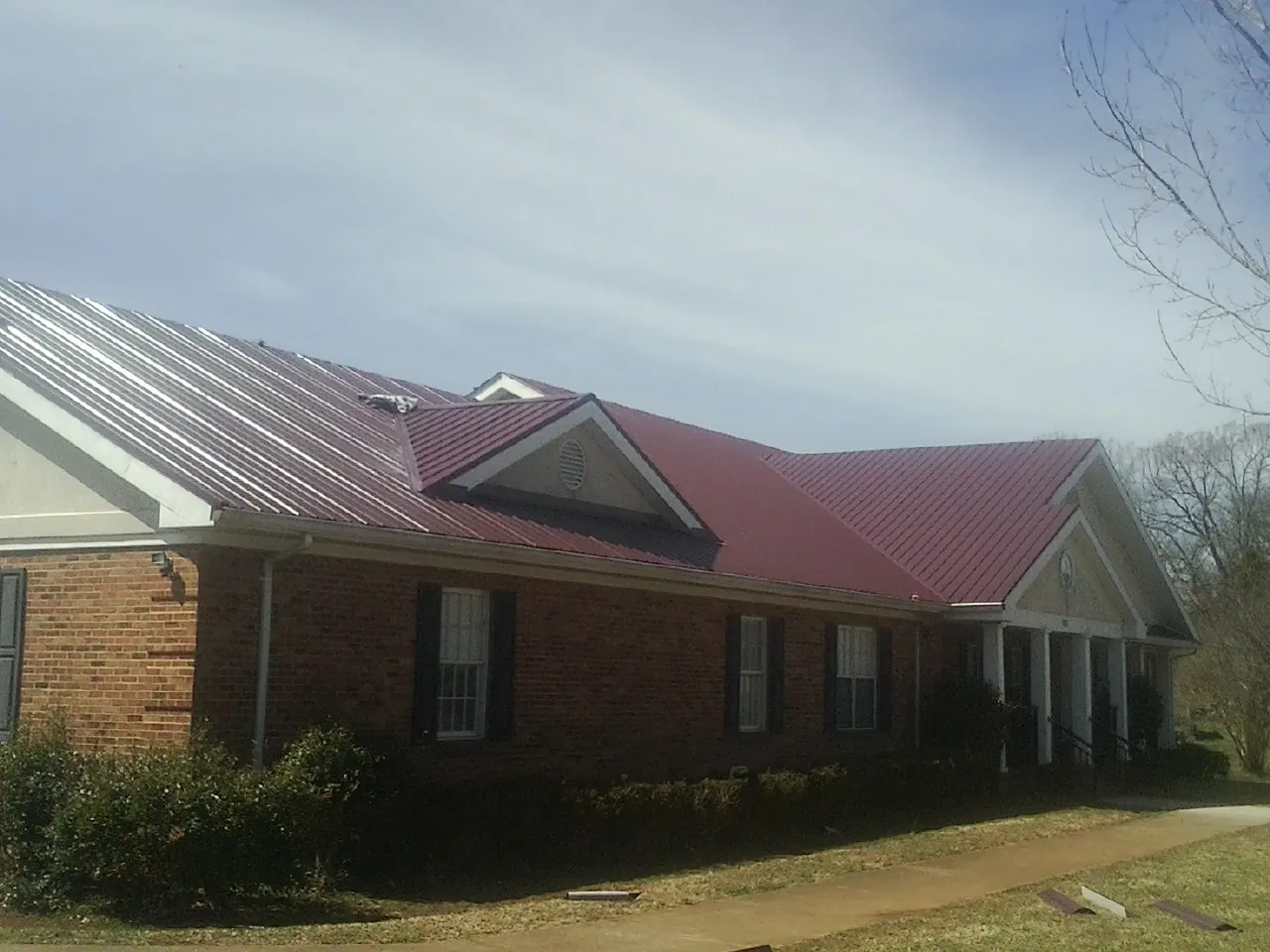 Red metal roof with gabled entries on a long brick building, from a Hail Damage Roof Repair job in Scottsville